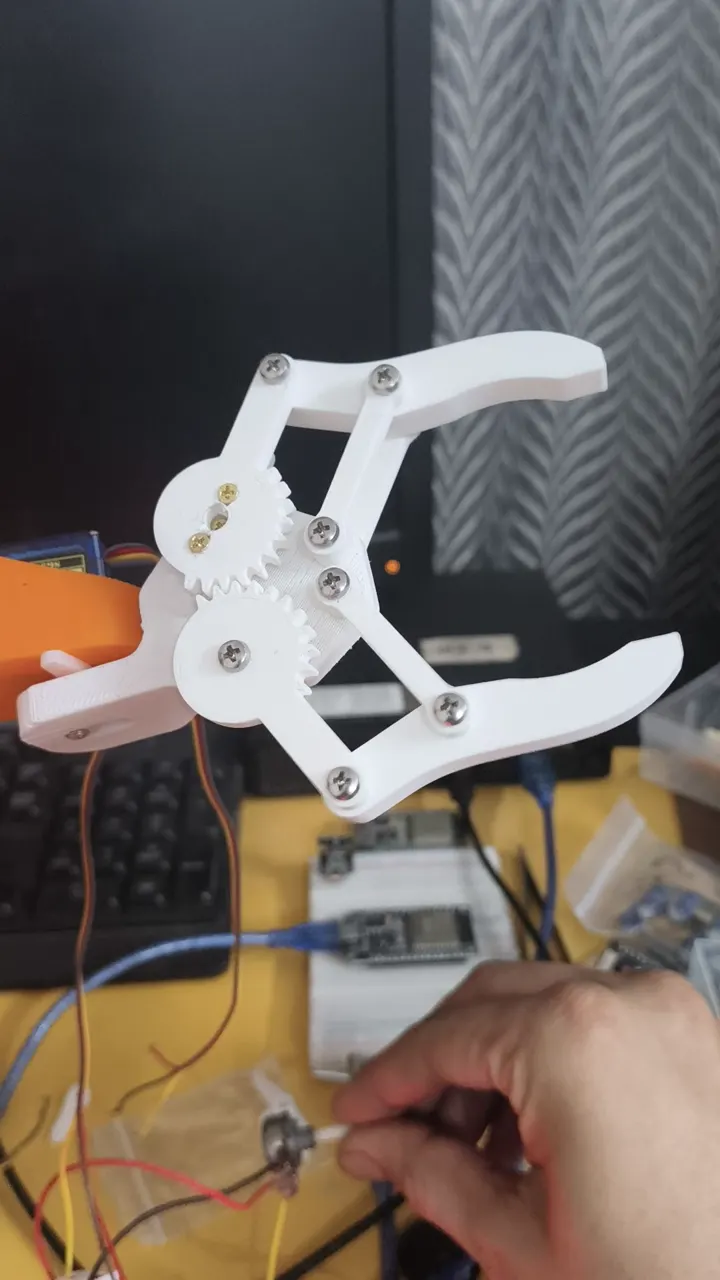 A white 3D-printed servo gripper being tested on a Makerhood workbench